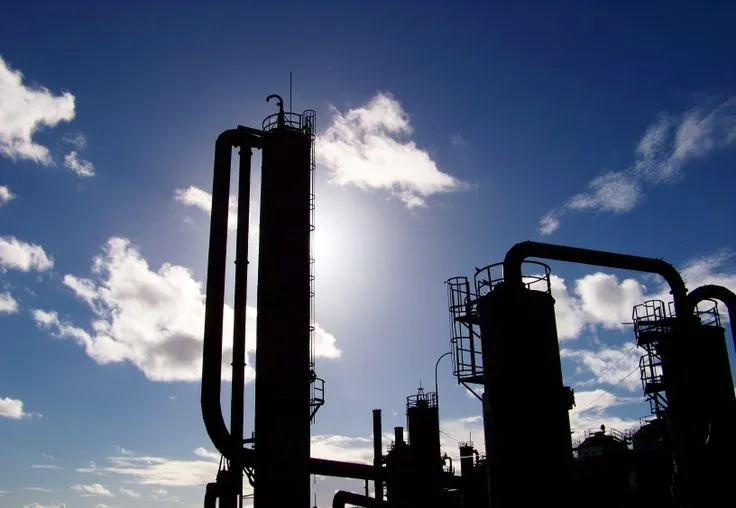 The cracking towers of Gas Works Park in black silhouette against a bright blue sky, sun burning through behind them