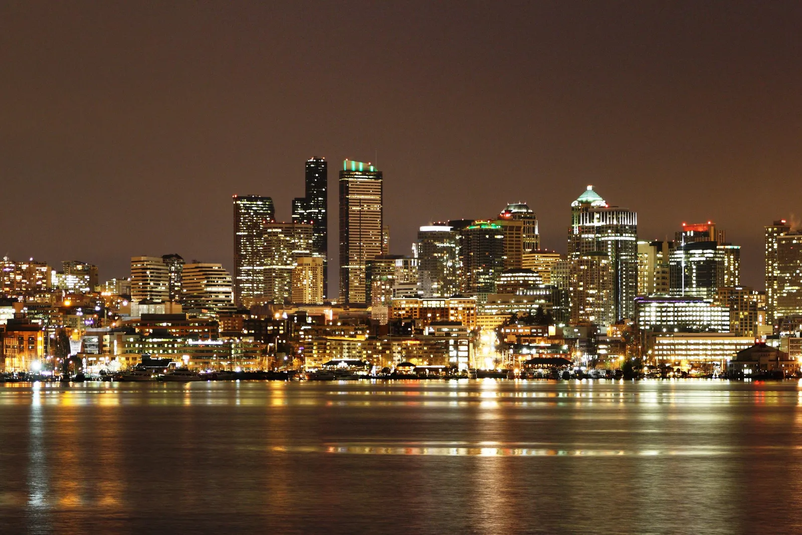 A wide night panorama across Lake Union from Gas Works Park, showing the lit downtown Seattle skyline, the Space Needle at the right, and houseboats and marinas along the far shore reflected in the water