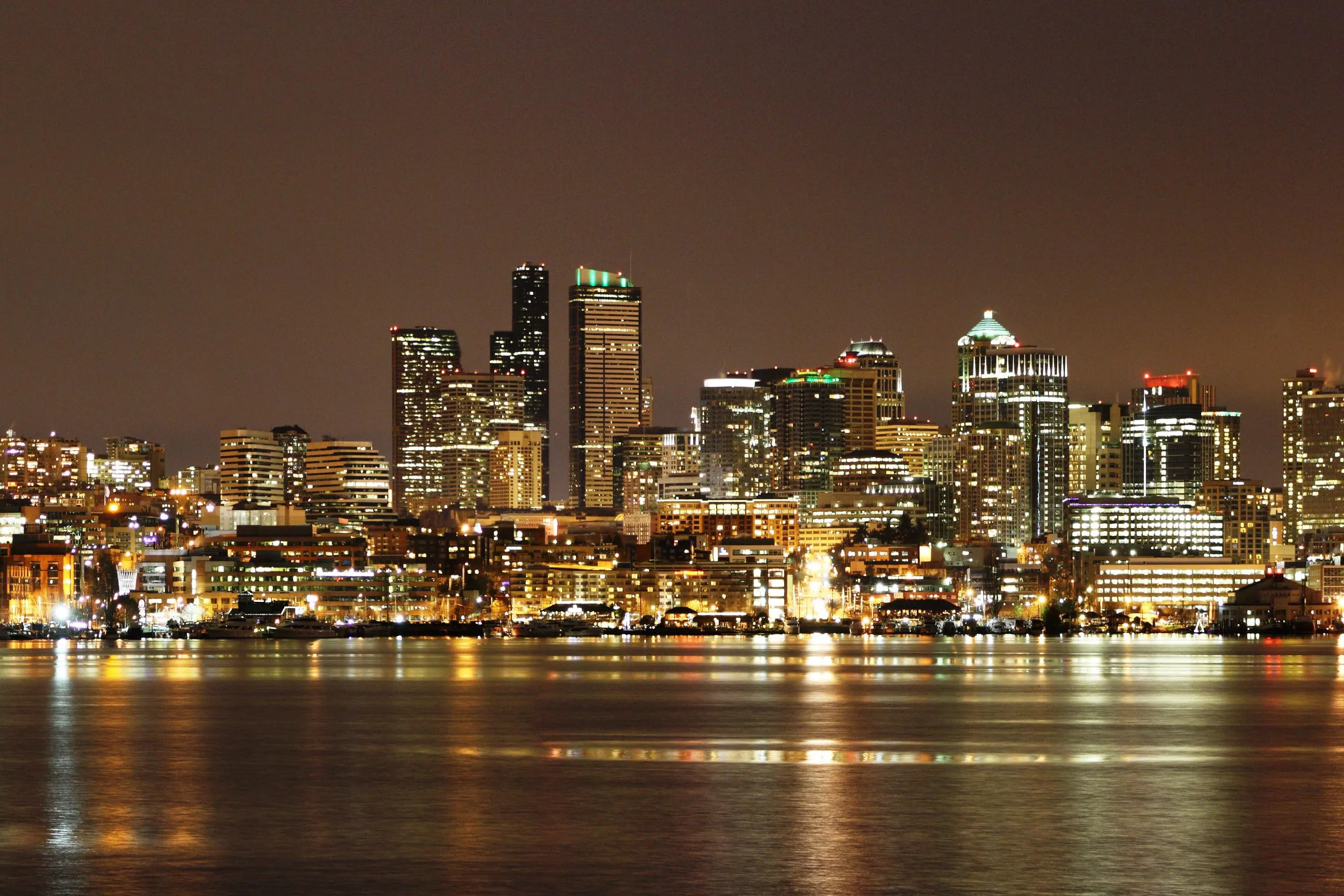 A wide night panorama across Lake Union from Gas Works Park, showing the lit downtown Seattle skyline, the Space Needle at the right, and houseboats and marinas along the far shore reflected in the water